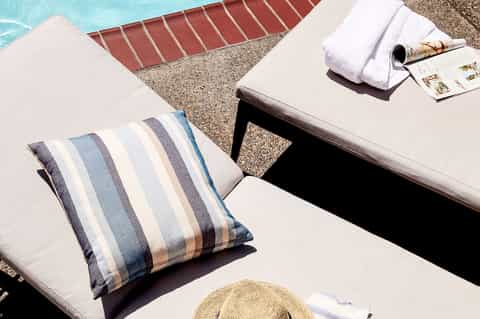 Poolside lounge chairs with striped pillows, towels, magazines, and turquoise pool visible