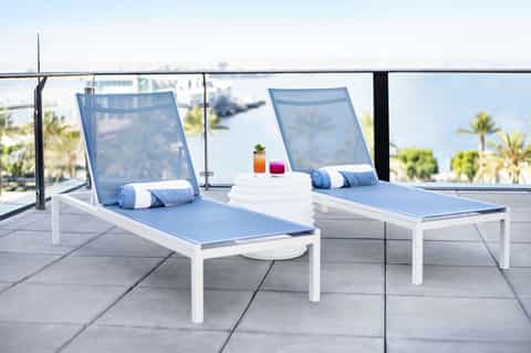 Rooftop lounge with two blue mesh chaise lounges overlooking palm trees and coastal city skyline