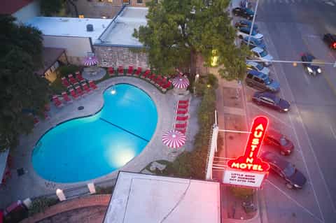 Aerial view of kidney-shaped pool with red loungers and pink neon motel sign on street