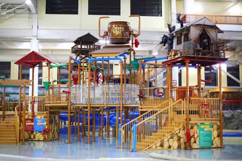 Indoor water park play structure with slides, climbing equipment, and lodge-themed architecture