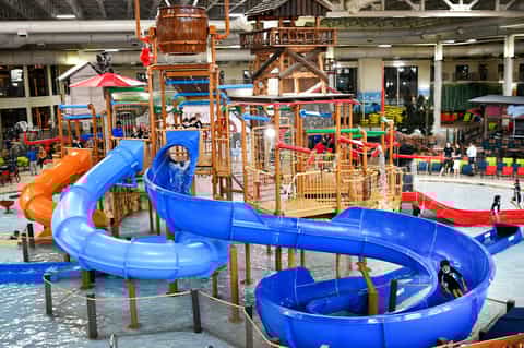 Indoor water park with large blue slides, wooden play structures, and children playing