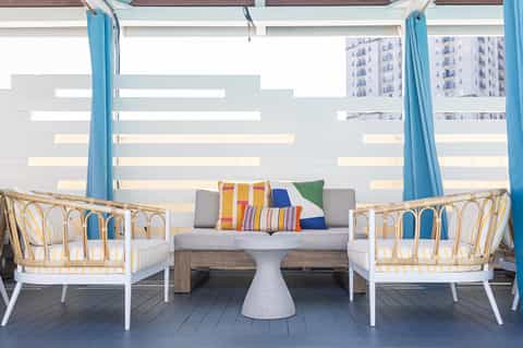 Modern resort balcony with rattan chairs, gray sofa, colorful pillows, and striped privacy screens