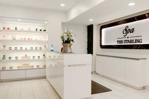 Spa reception area with white shelving displaying products, neon sign, and floral arrangement