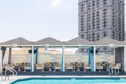 Urban rooftop pool with modern cabanas, mesh shade structures, and high-rise building view