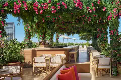 Rooftop bar with magenta bougainvillea pergola, wooden seating, and city skyline view