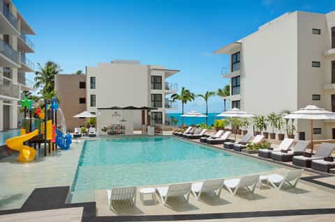 Family resort pool with waterslide, lounging areas, and ocean view in background