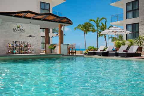Beachfront resort pool with swim-up bar, lounge chairs, umbrellas, and ocean horizon views
