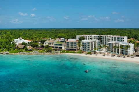 Modern beachfront resort with white buildings nestled between jungle and turquoise sea
