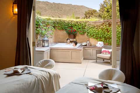 Luxury spa suite with outdoor soaking tub, ivy-covered walls, mountain backdrop, and bedroom lounge