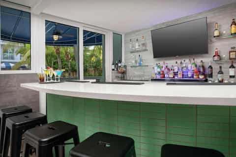 Contemporary bar lounge with curved white counter, colorful cocktails, green cabinetry, and tropical views