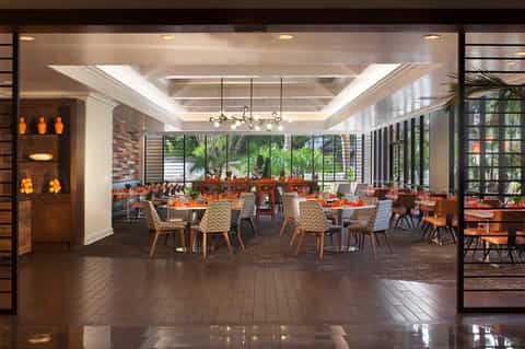 Modern hotel restaurant interior with tables, orange accents, and floor-to-ceiling windows