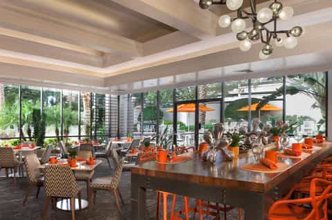 Elegant dining room with orange accents, modern lighting, and floor-to-ceiling windows