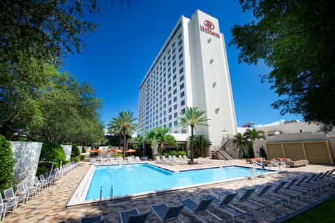 Resort pool surrounded by loungers and palm trees with tall white hotel building