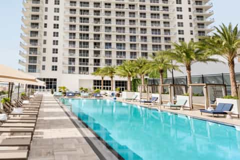 Modern high-rise hotel pool with turquoise water, loungers, palm trees, and tall residential building