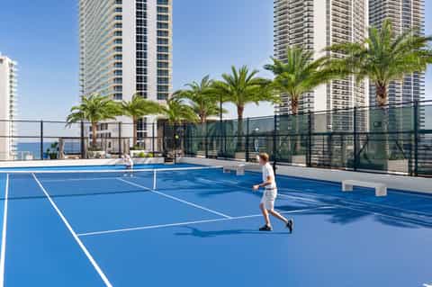 Rooftop tennis court with ocean views, surrounded by high-rise hotels and palm trees