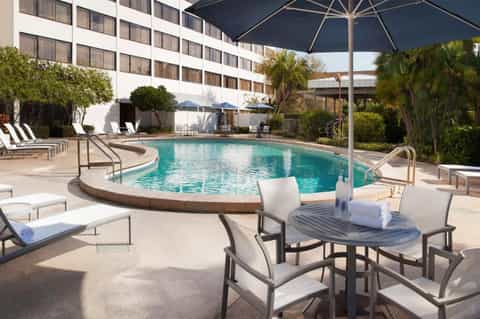 Resort pool with curved edges, lounge seating, umbrellas, and modern hotel building backdrop