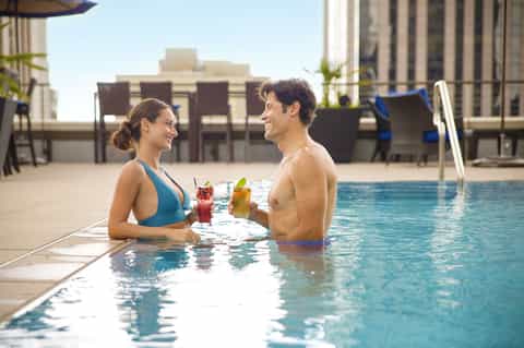Couple enjoying cocktails in an urban rooftop pool with city skyline backdrop