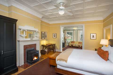 Luxury bedroom with fireplace, yellow walls, wooden desk, and sitting area with windows