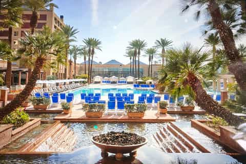 Luxurious resort pool courtyard with palm trees, blue lounge chairs, and water fountain surrounded by terracotta buildings