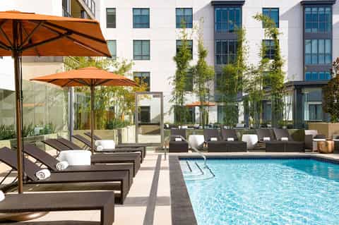 Resort pool with lounge chairs, orange umbrellas, and contemporary building with green climbing vines