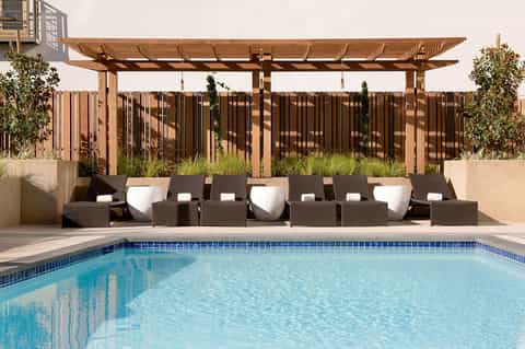 Luxury poolside lounge with rattan seating, white cushions, wooden pergola, and resort-style pool setting