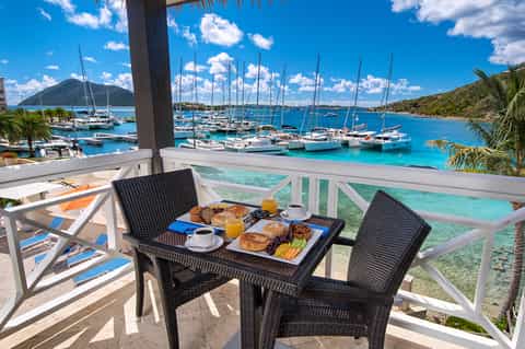 Beachfront balcony breakfast setup with ocean view, sailboats, and tropical bay scenery