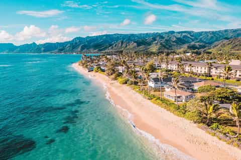 Aerial coastal view of tropical beach town with turquoise water and mountain backdrop