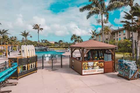 Lakeside resort area with water sports rental kiosk, palm trees, turquoise water, and hotel building