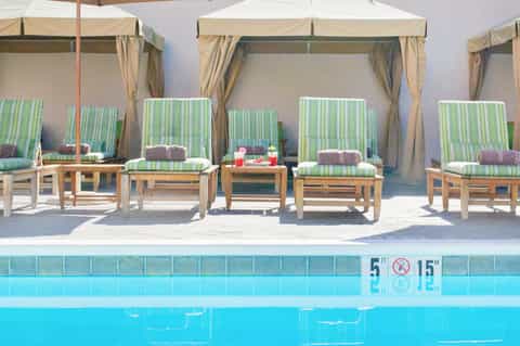 Poolside lounge area with green striped cabanas, white umbrellas, and crystal blue water
