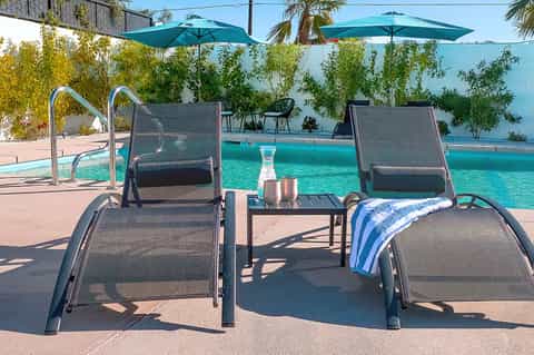 Resort pool deck with gray mesh loungers, teal umbrellas, turquoise water, and climbing vines