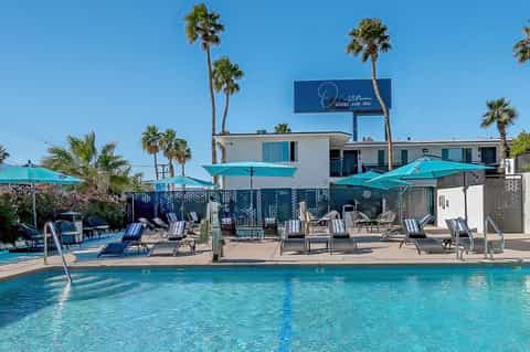 Resort pool area with turquoise umbrellas, lounge chairs, palm trees, and Orion Hotel and Spa building in background