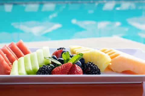 Colorful fruit platter with watermelon, cantaloupe, berries, and melon arranged on white plate by pool