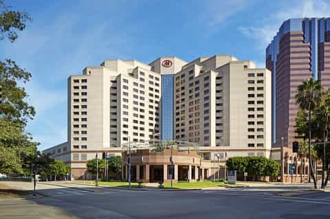 Multi-story beige hotel building with central tower and palm trees in plaza setting
