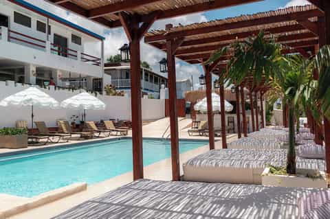 Resort pool with wooden pergola shade structures, lounge chairs, beach access, and tropical landscaping