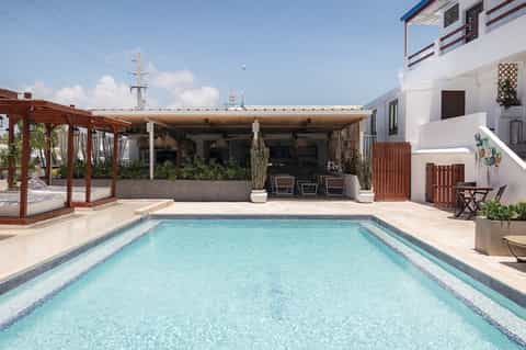 Rectangular resort pool with turquoise water, wooden pergola bar structure, and modern white building