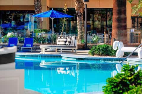 Luxurious poolside patio with blue umbrella, lounge chairs, and palm trees