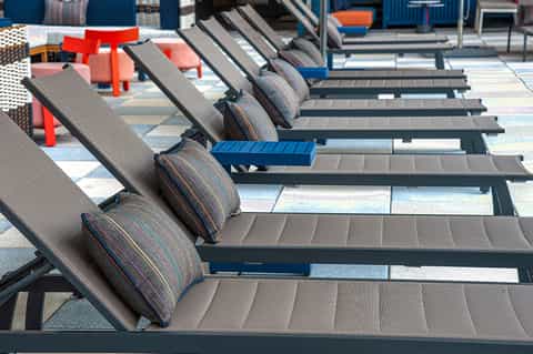 Resort pool deck with gray lounge chairs with striped cushions and colorful accent furniture