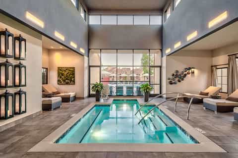 Modern indoor lap pool with floor-to-ceiling windows, lounge seating, and contemporary wellness facility design