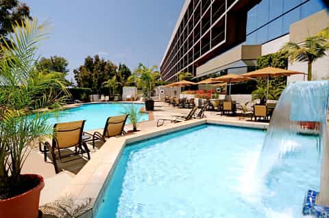 Resort pool and spa with lounge chairs, umbrellas, and modern hotel building