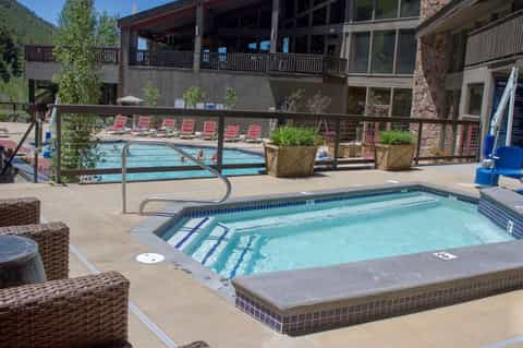 Mountain resort pool area with hot tub, red loungers, and multi-level wooden lodge building