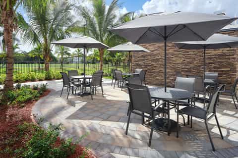 Outdoor patio with black lounge chairs, gray umbrellas, palm trees, and stone accent wall