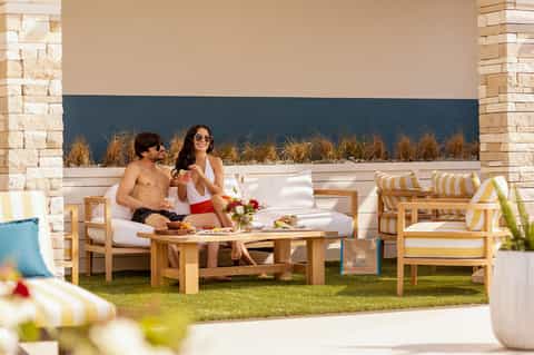 Couple relaxing on a beachfront lounge with white cushions and striped pillows, ocean view