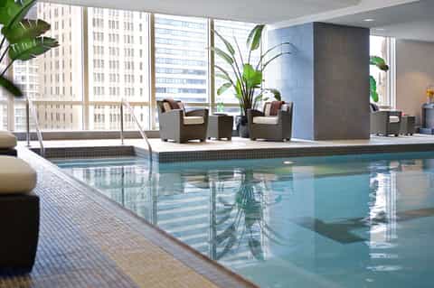 Indoor hotel pool with city skyline views, lounge seating, and lush tropical plants