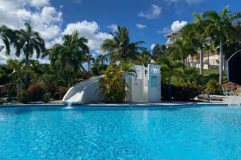 Waterslide feature in bright blue pool with palm trees and resort buildings on hillside