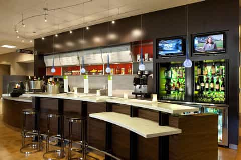 Modern hotel bar with dark wood counter, pendant lighting, and beverage display refrigerators