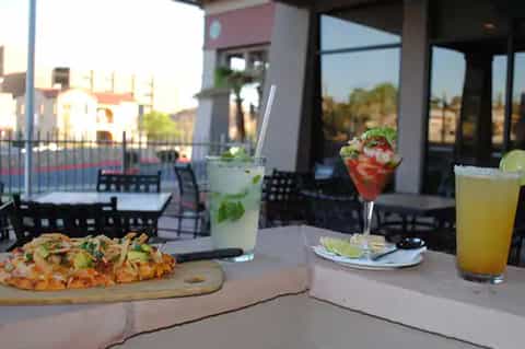 Outdoor dining area with cocktails, pizza, and sunset views from terrace