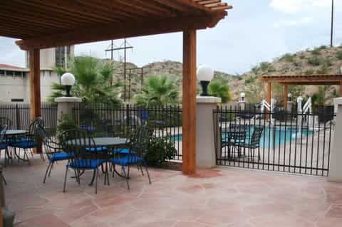 Covered patio seating area with wooden pergola, metal chairs, and pool view beyond fence