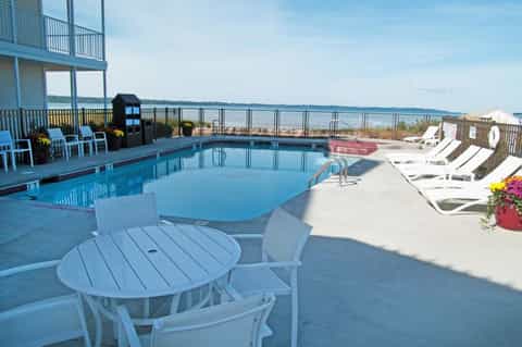 Oceanfront pool with ocean views, white lounge chairs, and multi-story beachfront building