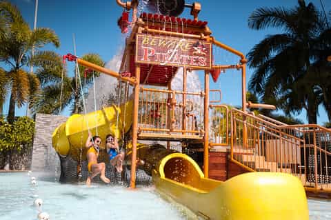 Family enjoying pirate ship water play structure with yellow slide and water fountains
