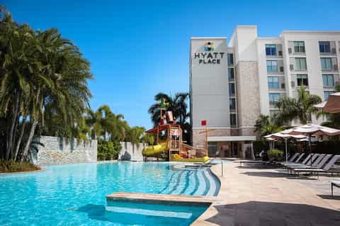 Family-friendly resort pool with waterslide, Hyatt Place hotel building, and palm trees